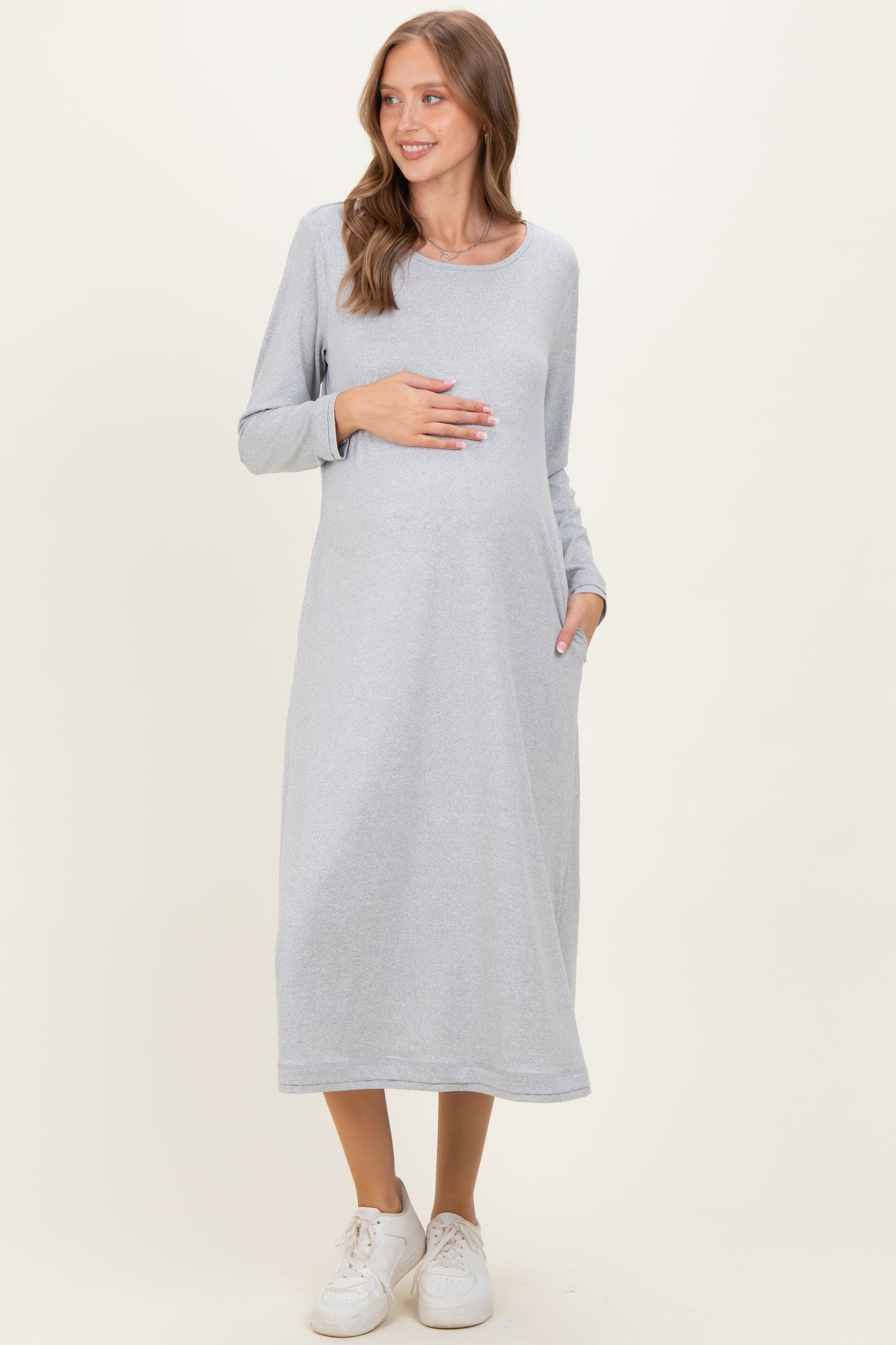 woman wearing a gray long sleeve maternity dress with pockets and holding her baby bump