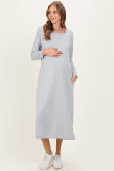 woman wearing a gray long sleeve maternity dress with pockets and holding her baby bump