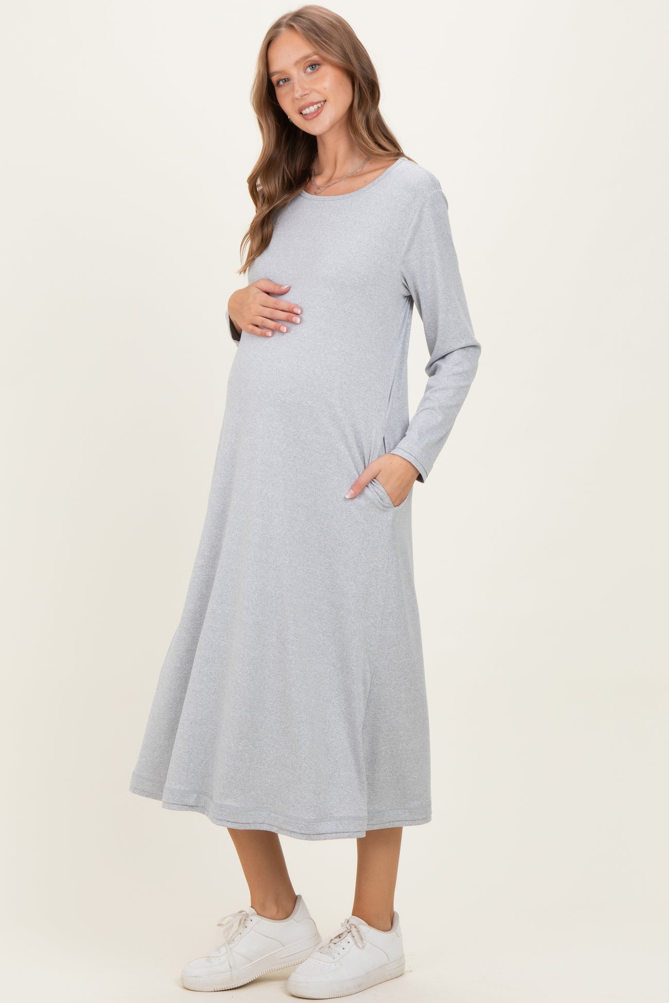 woman wearing a grey long sleeve maternity dress with pockets and holding her baby bump