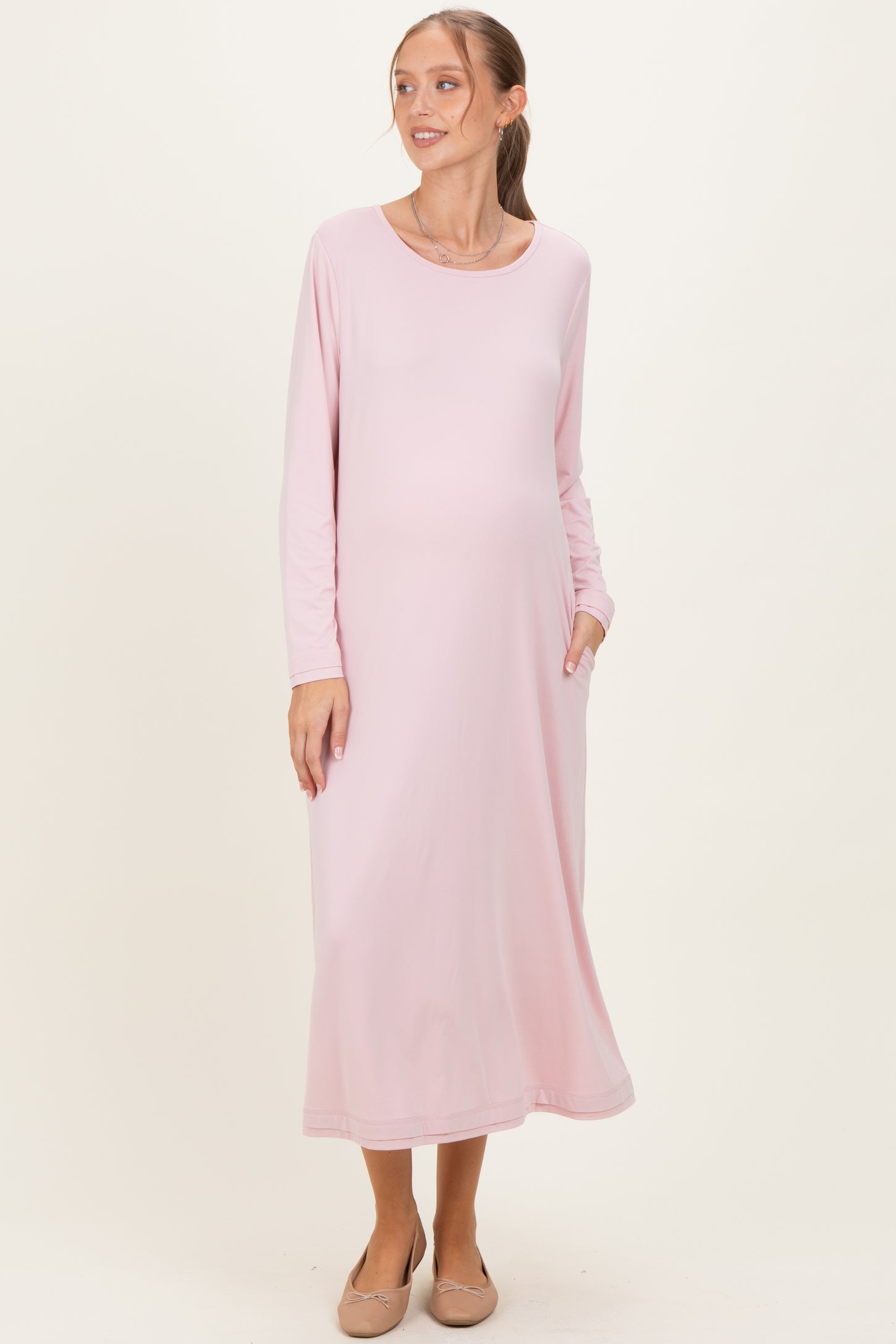 woman wearing a pink long sleeve maternity dress with pockets and a visible baby bump