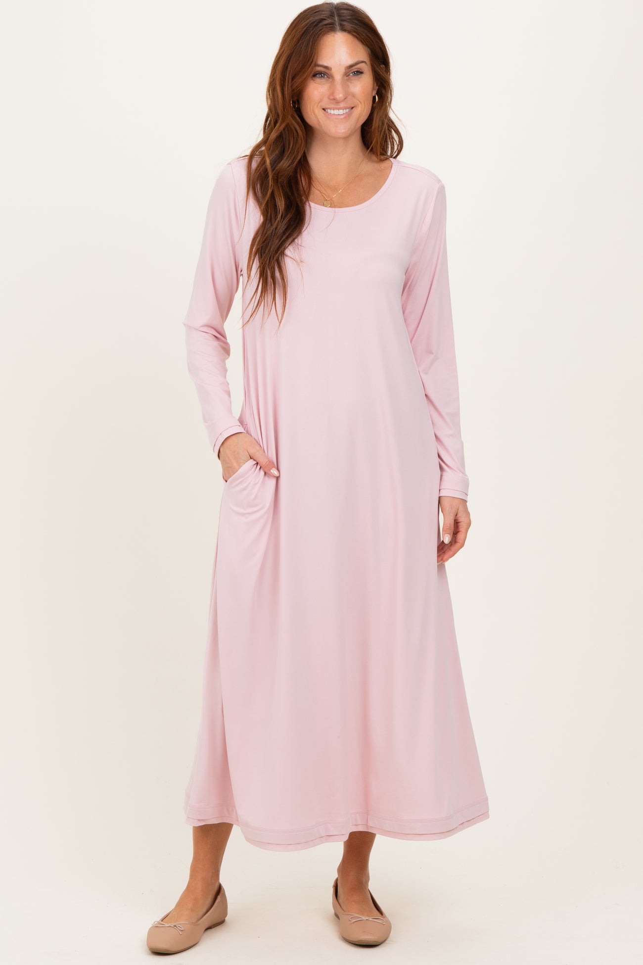 woman wearing a light pink long sleeve maxi dress with side pockets and a relaxed fit
