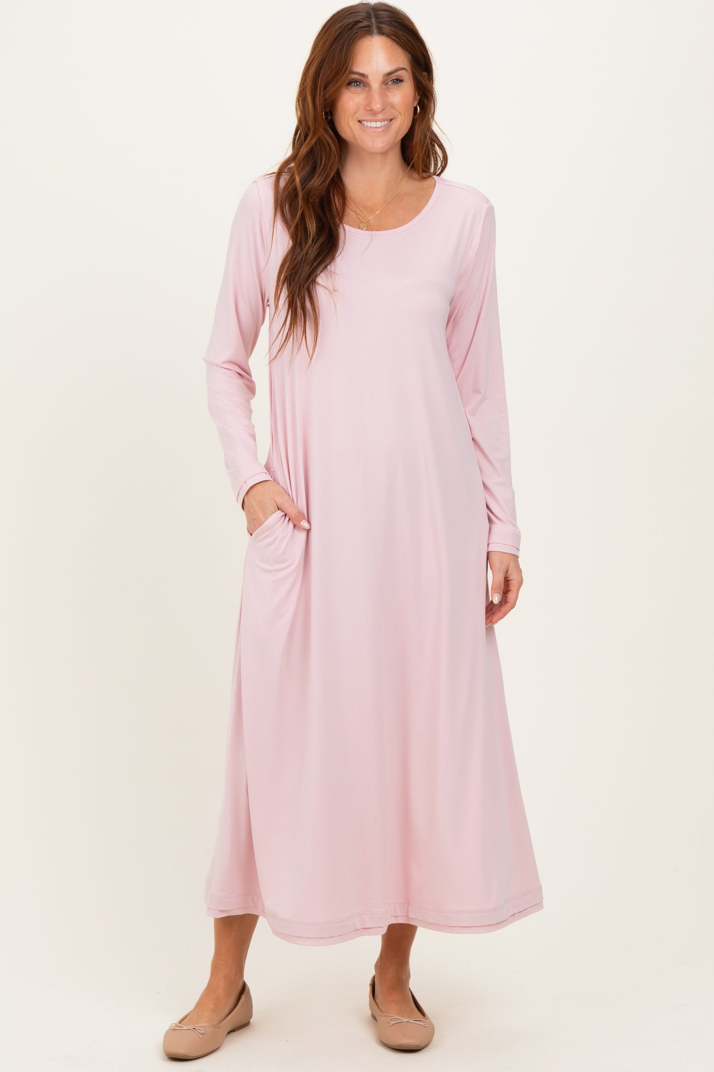 woman wearing a light pink long sleeve maxi dress with side pockets and a relaxed fit