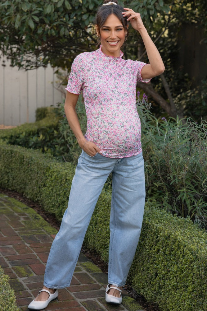 woman wearing a pink floral maternity top and light blue wide-leg jeans, showing off her baby bump outdoors