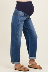 woman wearing maternity blue distressed straight-leg jeans with a black over-the-bump panel and brown sandals, showing baby bump