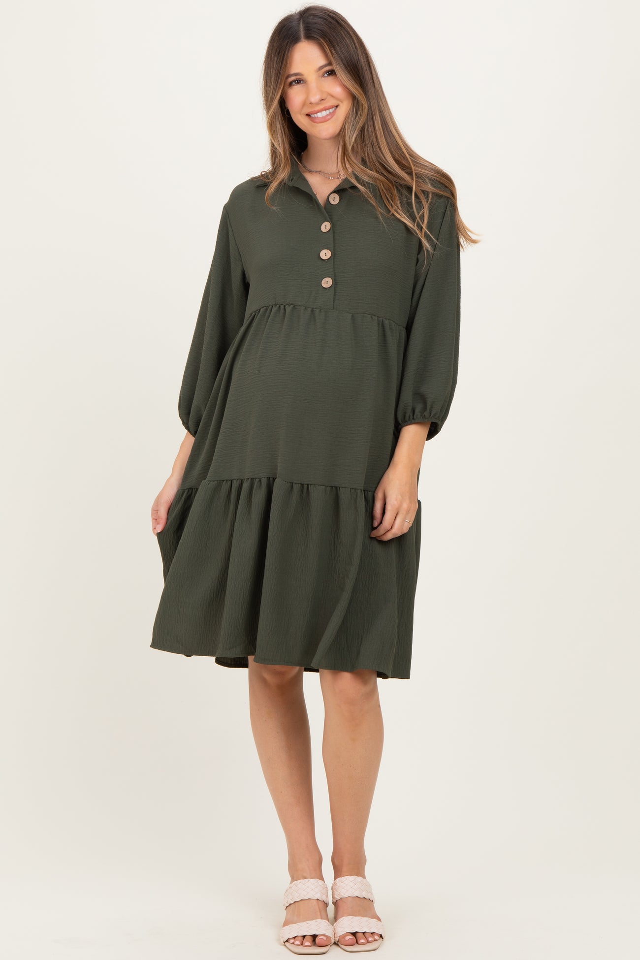 woman wearing a dark green maternity dress with puff sleeves and button details, standing with a baby bump visible