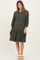 woman wearing a dark green maternity dress with puff sleeves and button details, standing with a baby bump visible