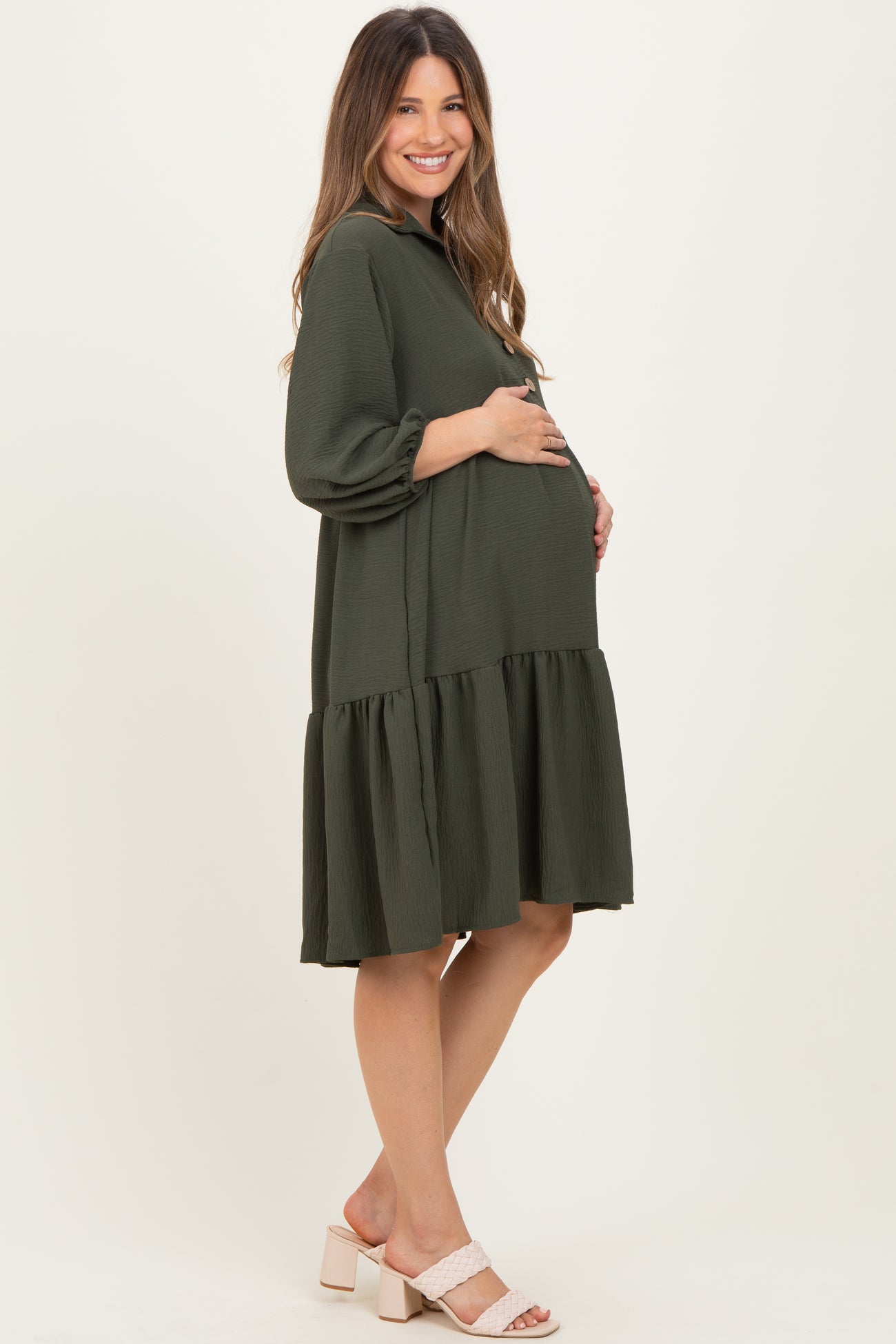 woman wearing a dark green maternity dress with a tiered skirt and a visible baby bump