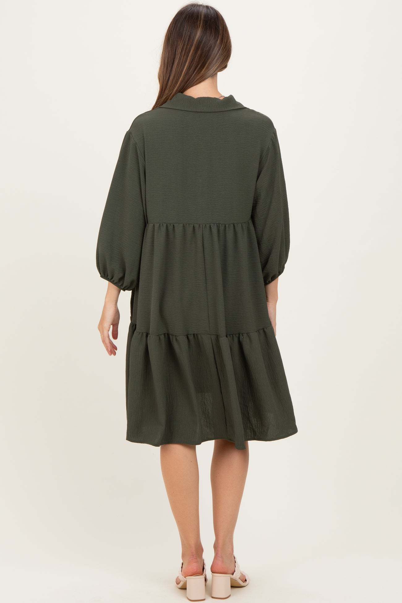 woman wearing a dark green maternity dress with puff sleeves and a tiered design, seen from the back