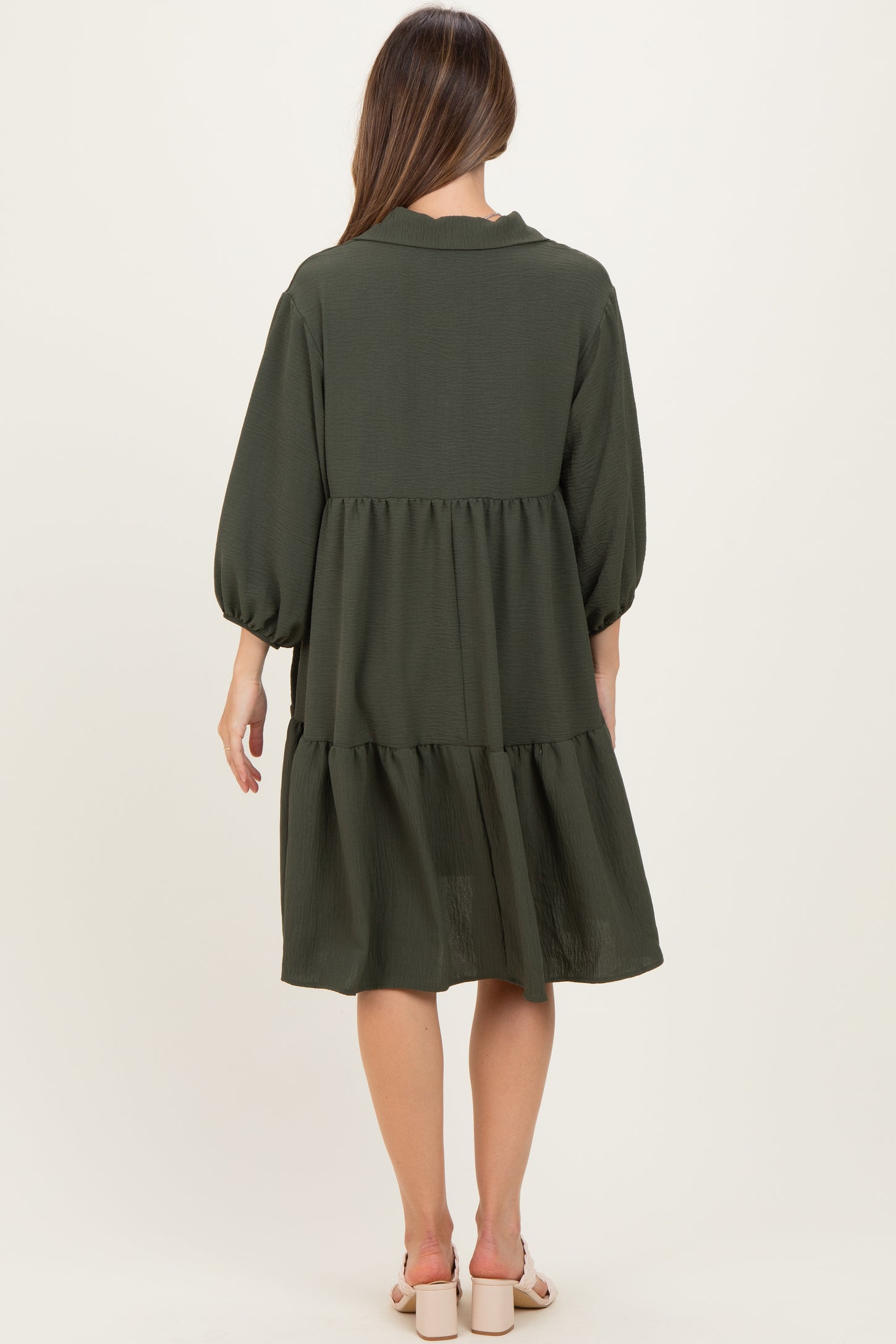 woman wearing a dark green maternity dress with puff sleeves and a tiered design, seen from the back