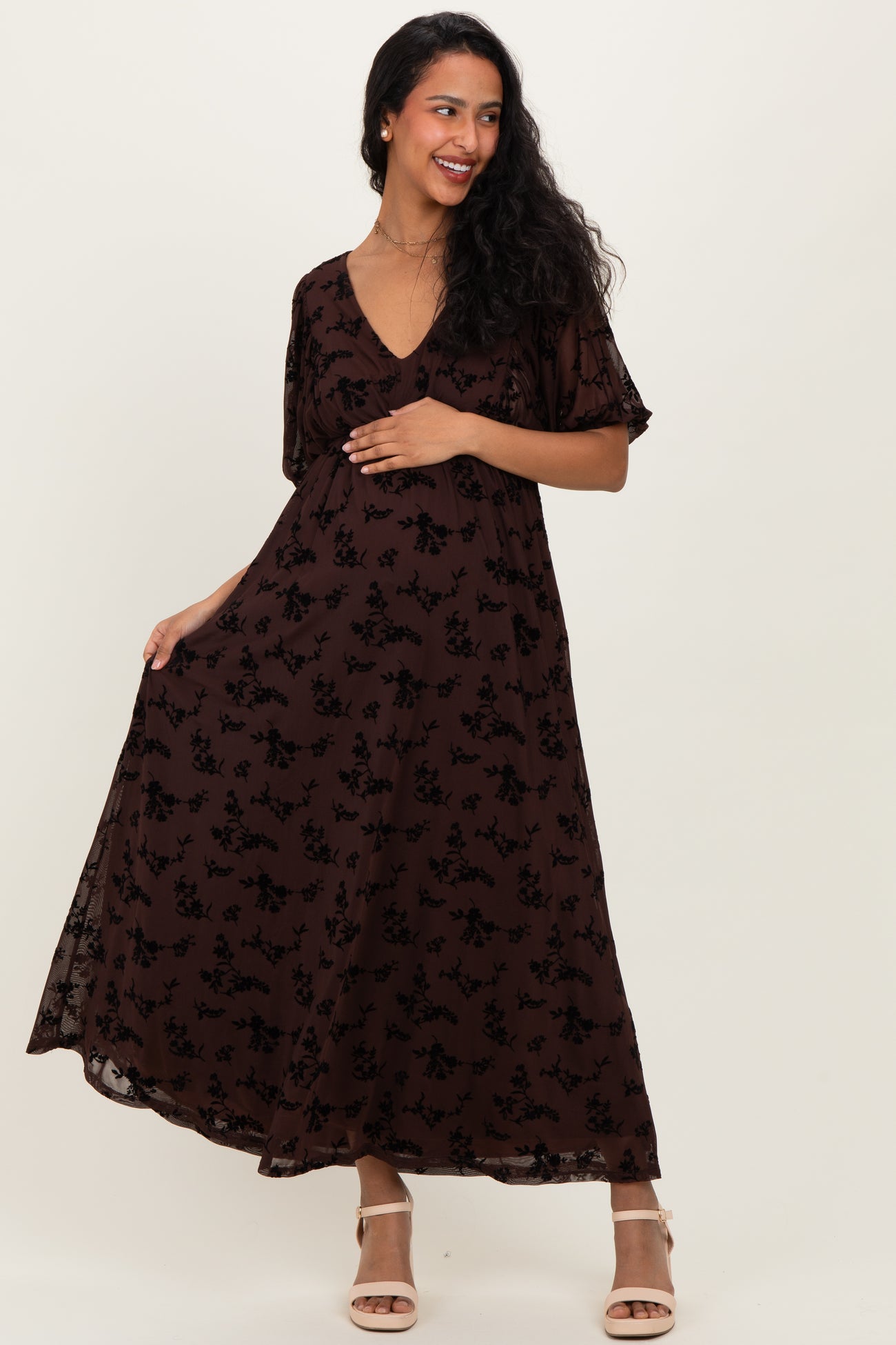 woman wearing a brown floral maternity maxi dress with short sleeves and a v-neckline, showcasing her baby bump