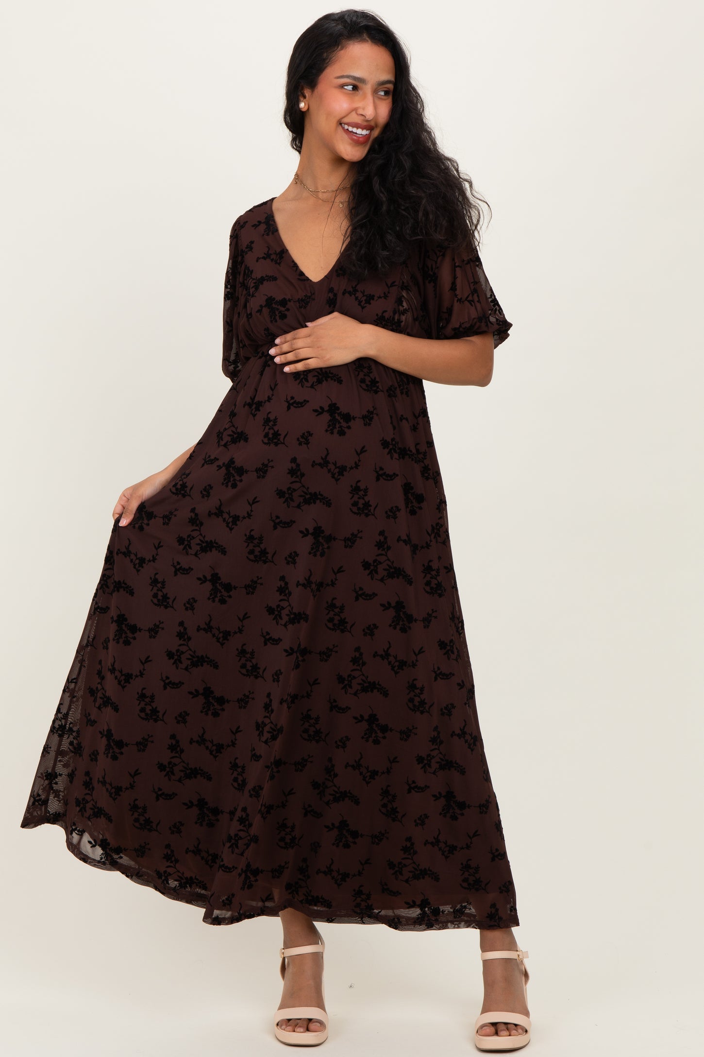 woman wearing a brown floral maternity maxi dress with short sleeves and a v-neckline, showcasing her baby bump