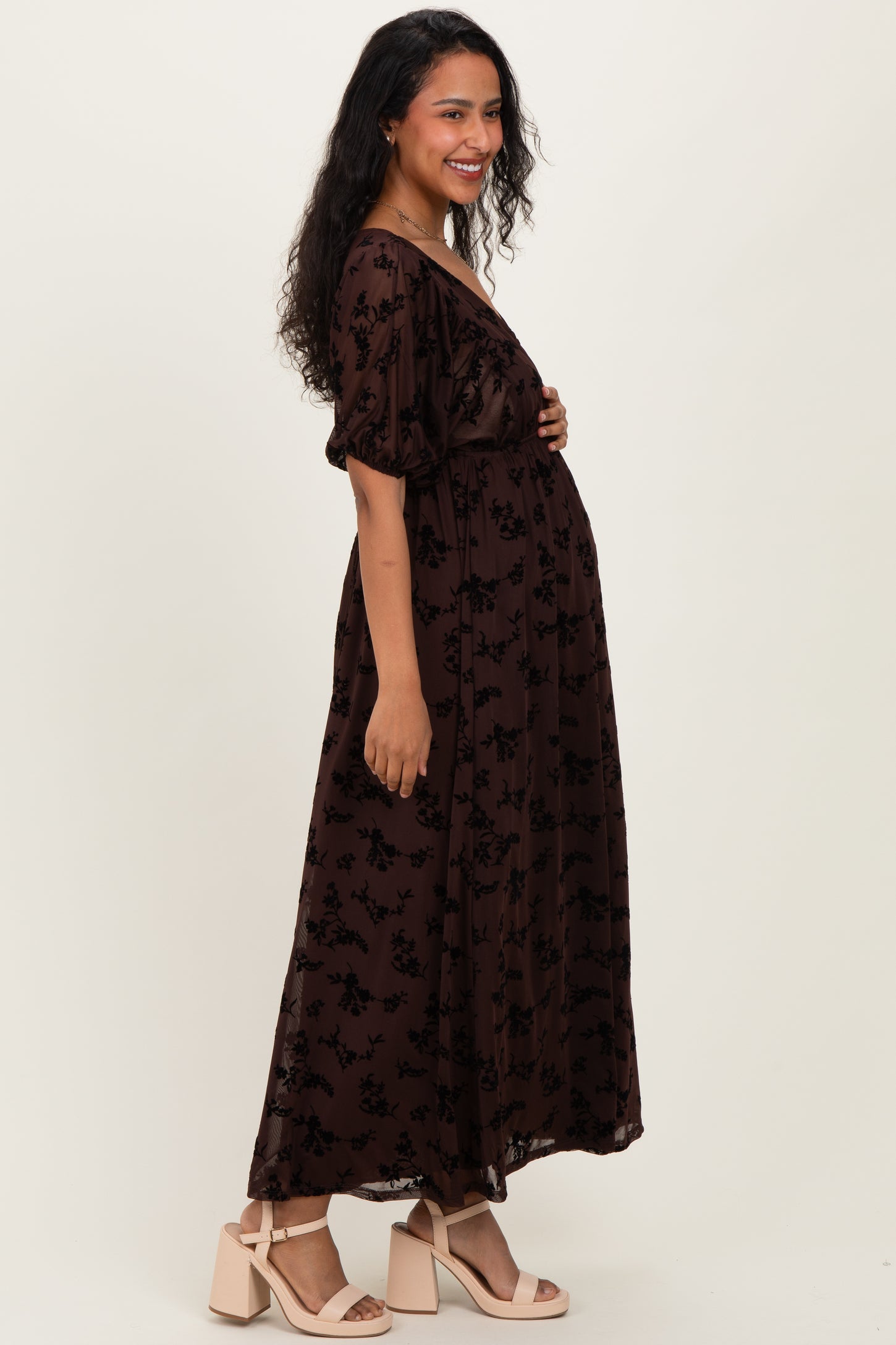 woman wearing a dark brown floral maternity dress with puff sleeves and a baby bump visible