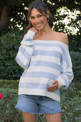 woman wearing a striped off-the-shoulder maternity sweater and denim shorts, holding her baby bump