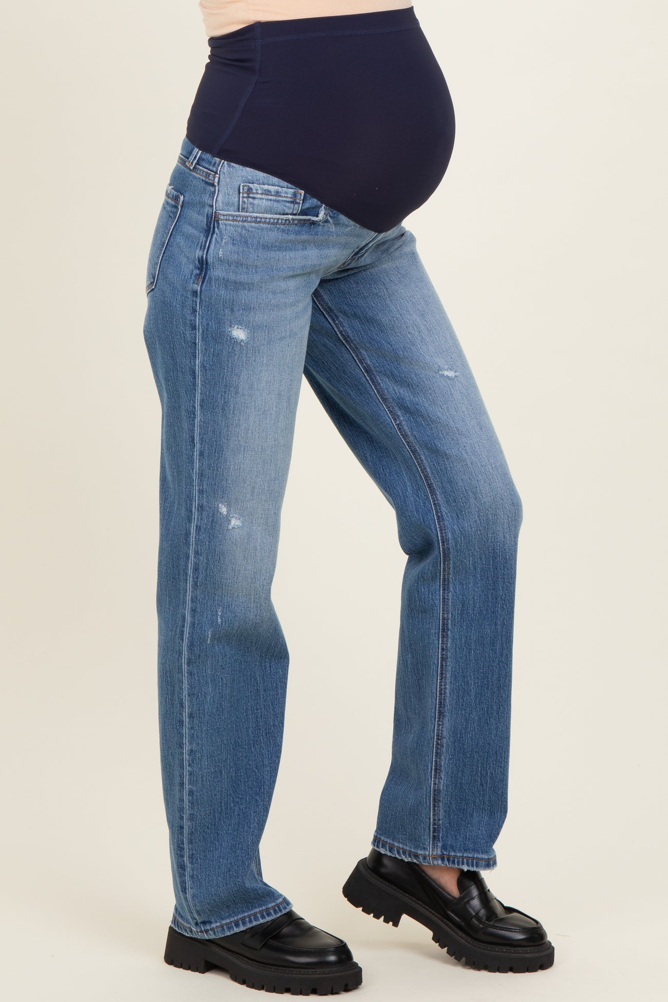 woman wearing light blue distressed maternity jeans with a dark blue over-the-bump waistband and a visible baby bump