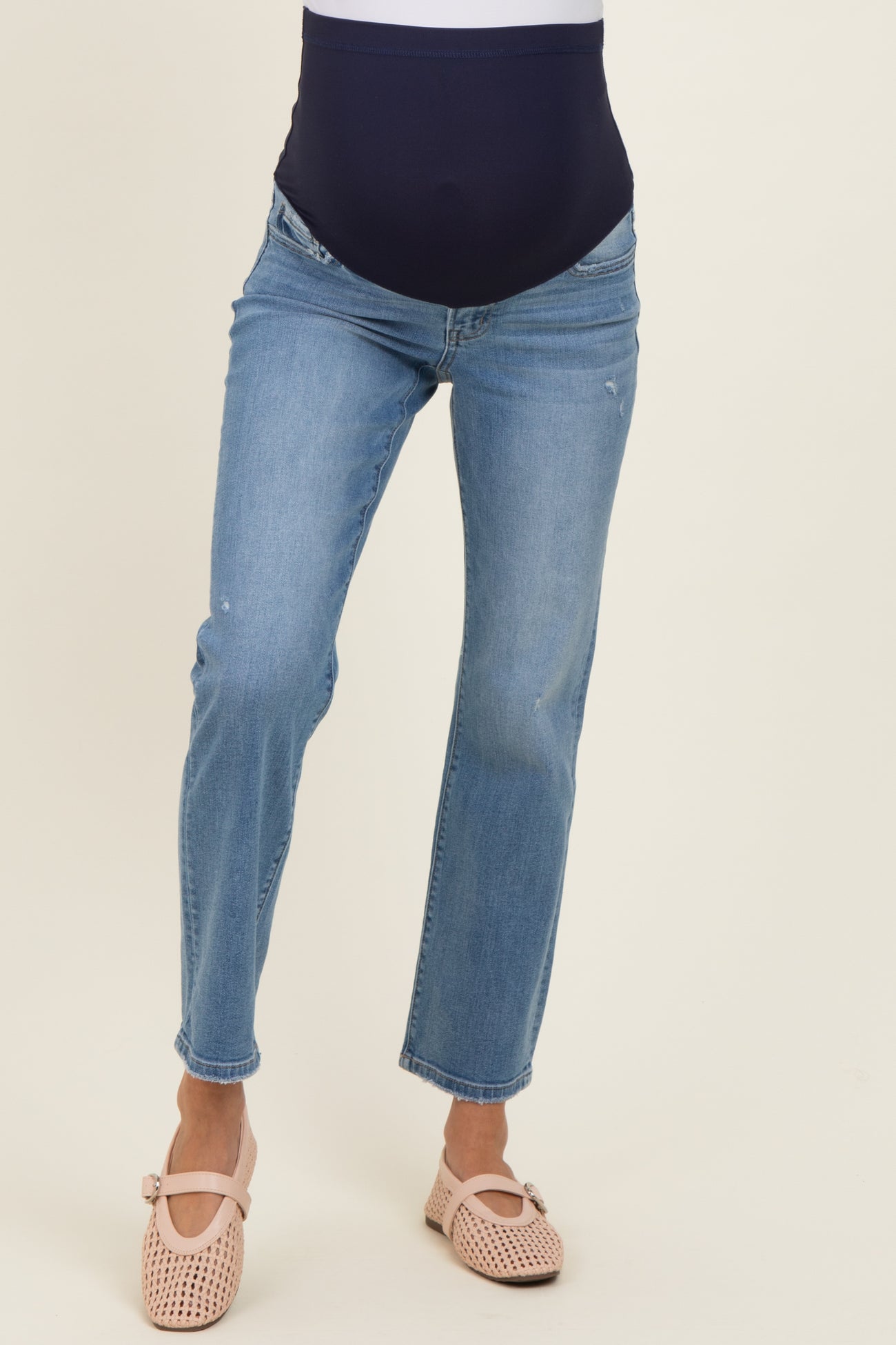 woman wearing light blue maternity jeans with a dark blue over-the-bump waistband and beige slip-on shoes