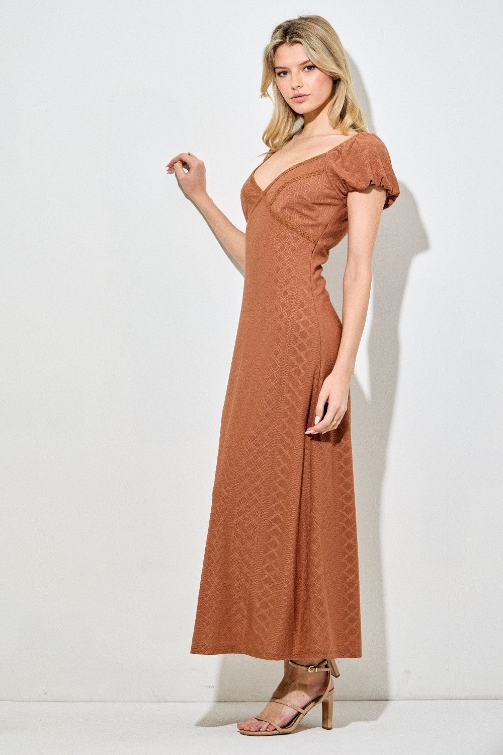 woman wearing a rust-colored maxi dress with short puff sleeves and a v-neckline, posing against a neutral background