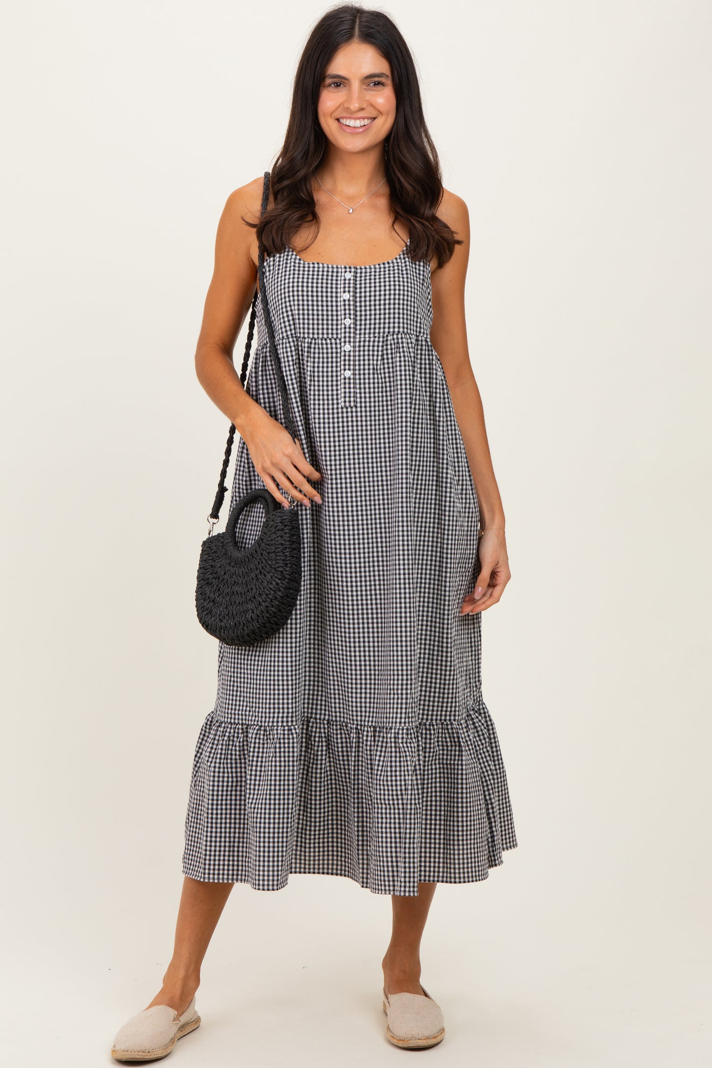 woman wearing a black and white gingham midi dress with buttons and a ruffle hem, holding a black woven bag