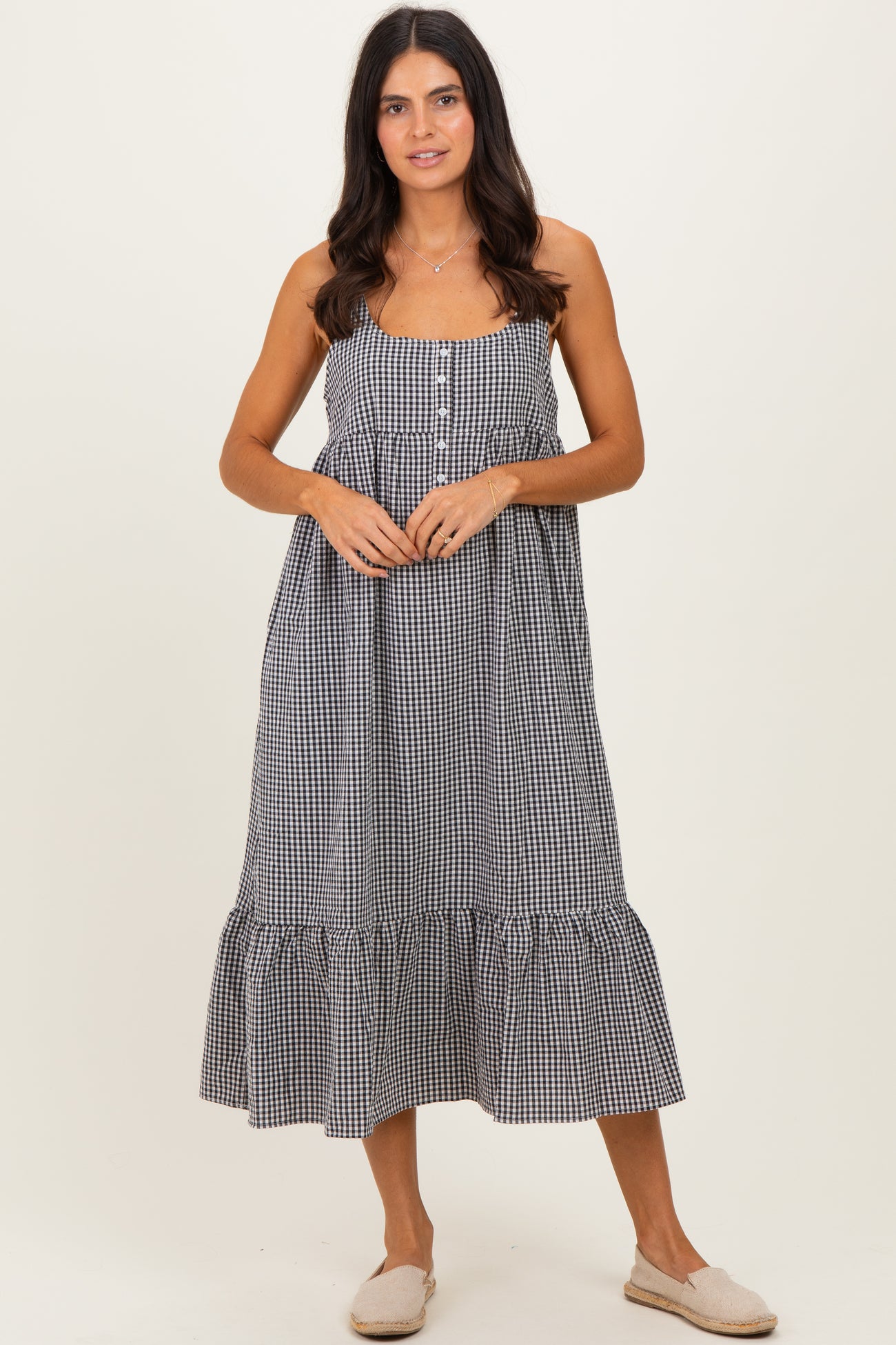woman wearing a black and white gingham maxi dress with buttons and a ruffled hem, standing on a neutral background
