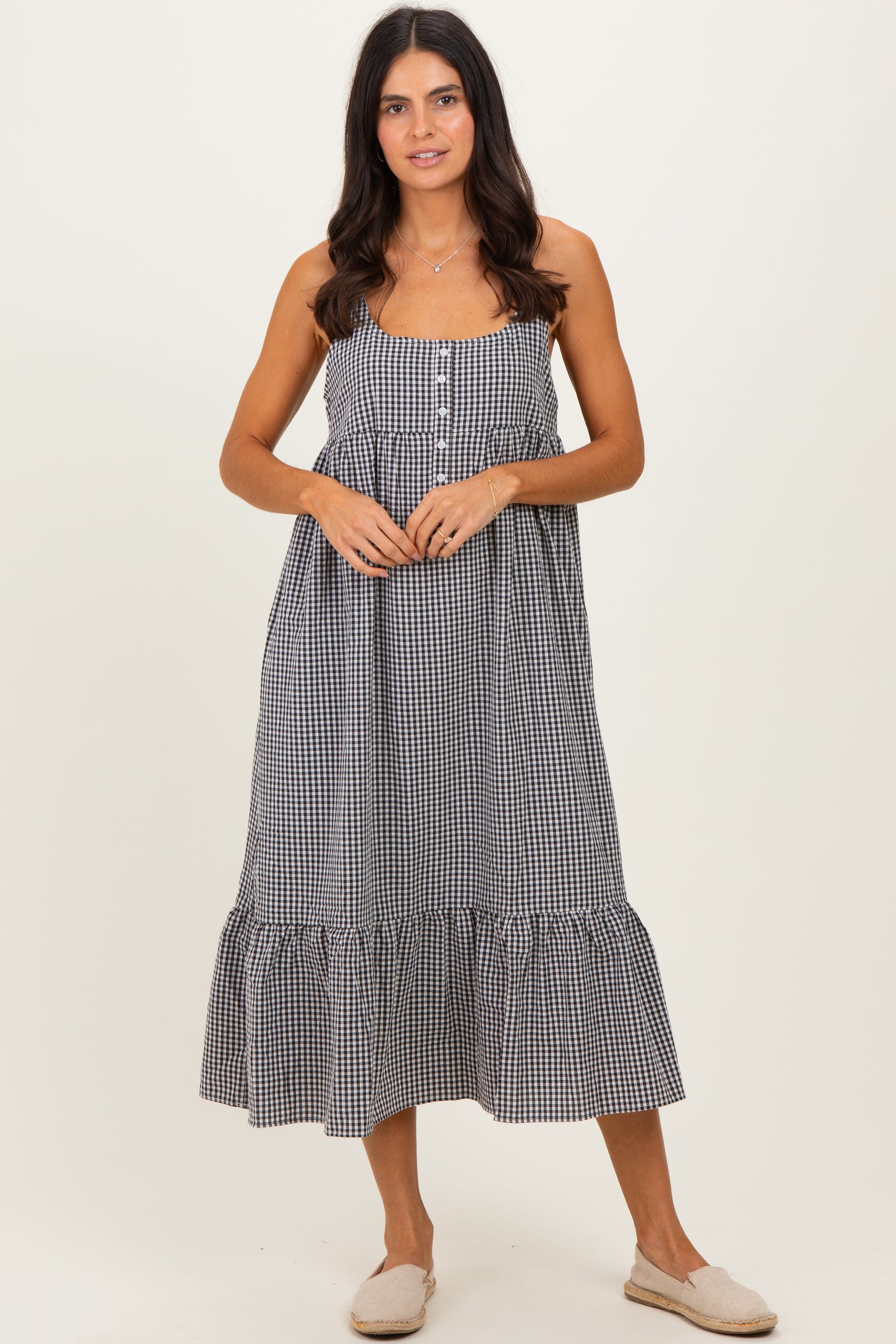 woman wearing a black and white gingham maxi dress with buttons and a ruffled hem, standing on a neutral background