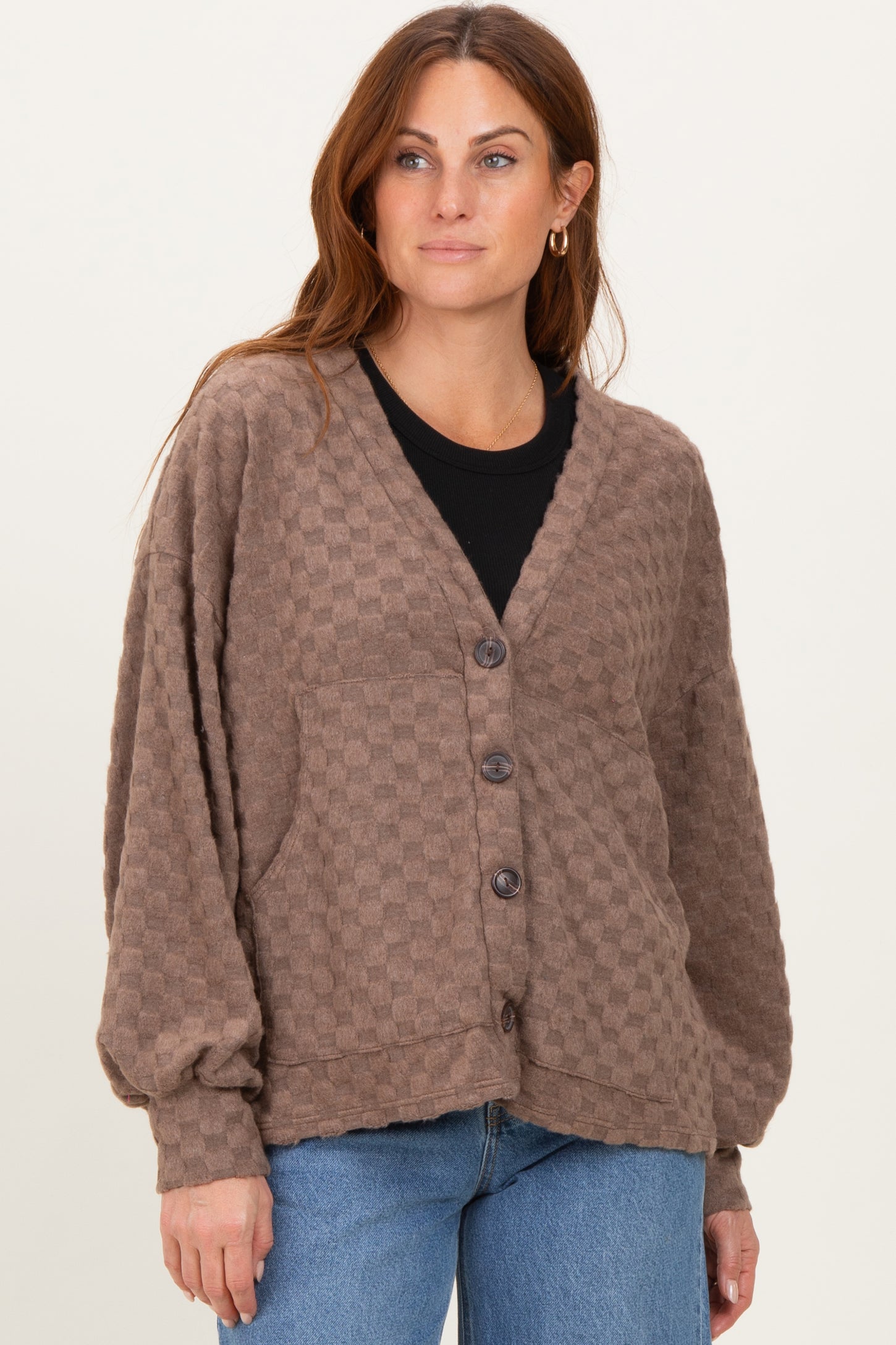 woman wearing a brown checkered cardigan with a deep v-neck and buttons, paired with a black top and blue jeans