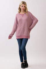 woman wearing a pink and white striped oversized sweatshirt with a v-neck and long sleeves, paired with blue jeans