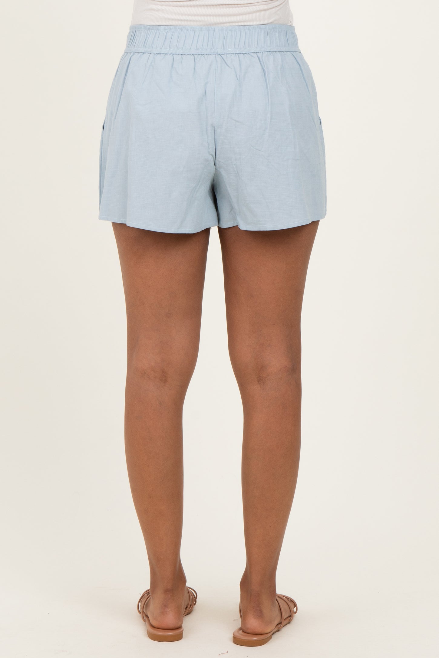 woman wearing light blue maternity shorts, featuring an elastic waistband and pockets, with a view of the back