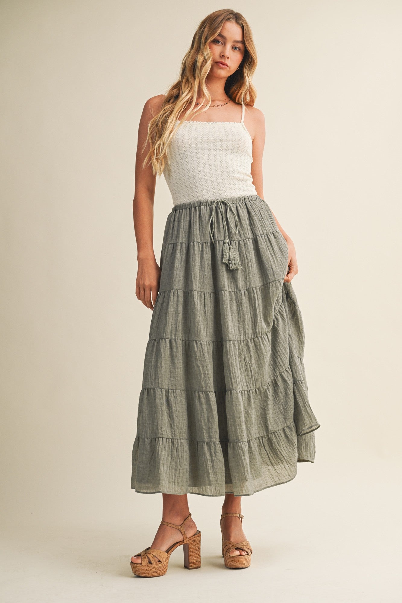 woman wearing a white smocked crop top and a long olive green tiered maxi skirt with tassel detail