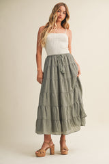 woman wearing a white smocked crop top and a long olive green tiered maxi skirt with tassel detail