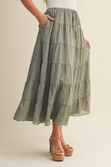 woman wearing a tiered olive green maxi skirt with pockets and a smocked waistband, paired with platform espadrilles