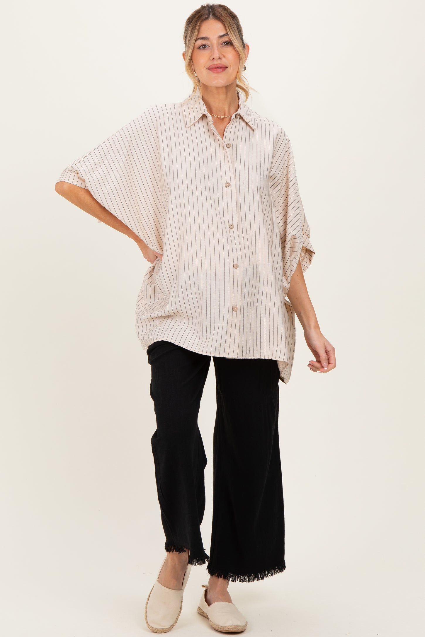woman wearing a striped oversized button-up maternity shirt and black wide-leg pants, showing her baby bump