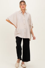 woman wearing a striped oversized button-up maternity shirt and black wide-leg pants, showing her baby bump