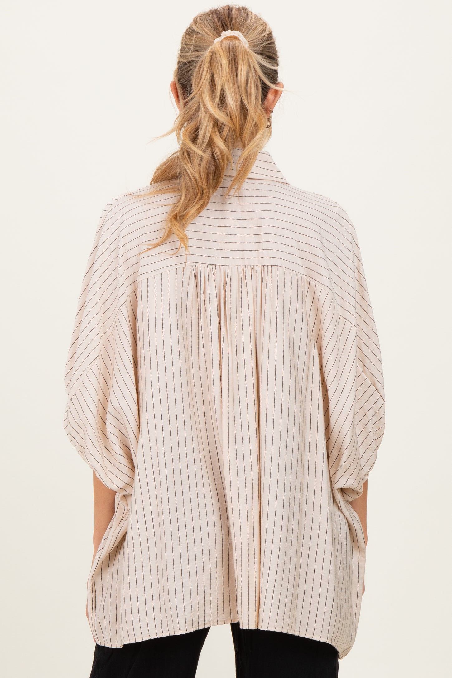 woman wearing a light beige maternity top with vertical stripes and a loose, oversized fit seen from the back