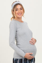 woman wearing a gray long sleeve maternity top and holding her baby bump, styled with a headband