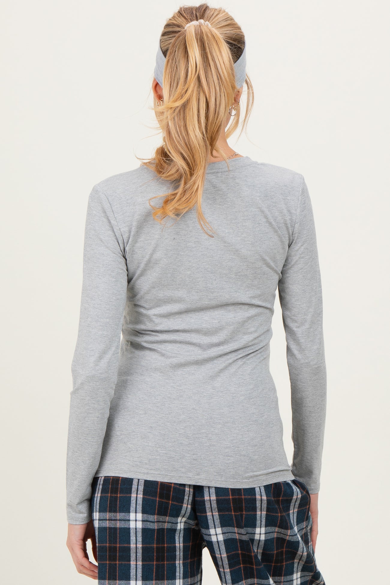 woman wearing a gray long sleeve maternity top, seen from the back, paired with plaid pajamas