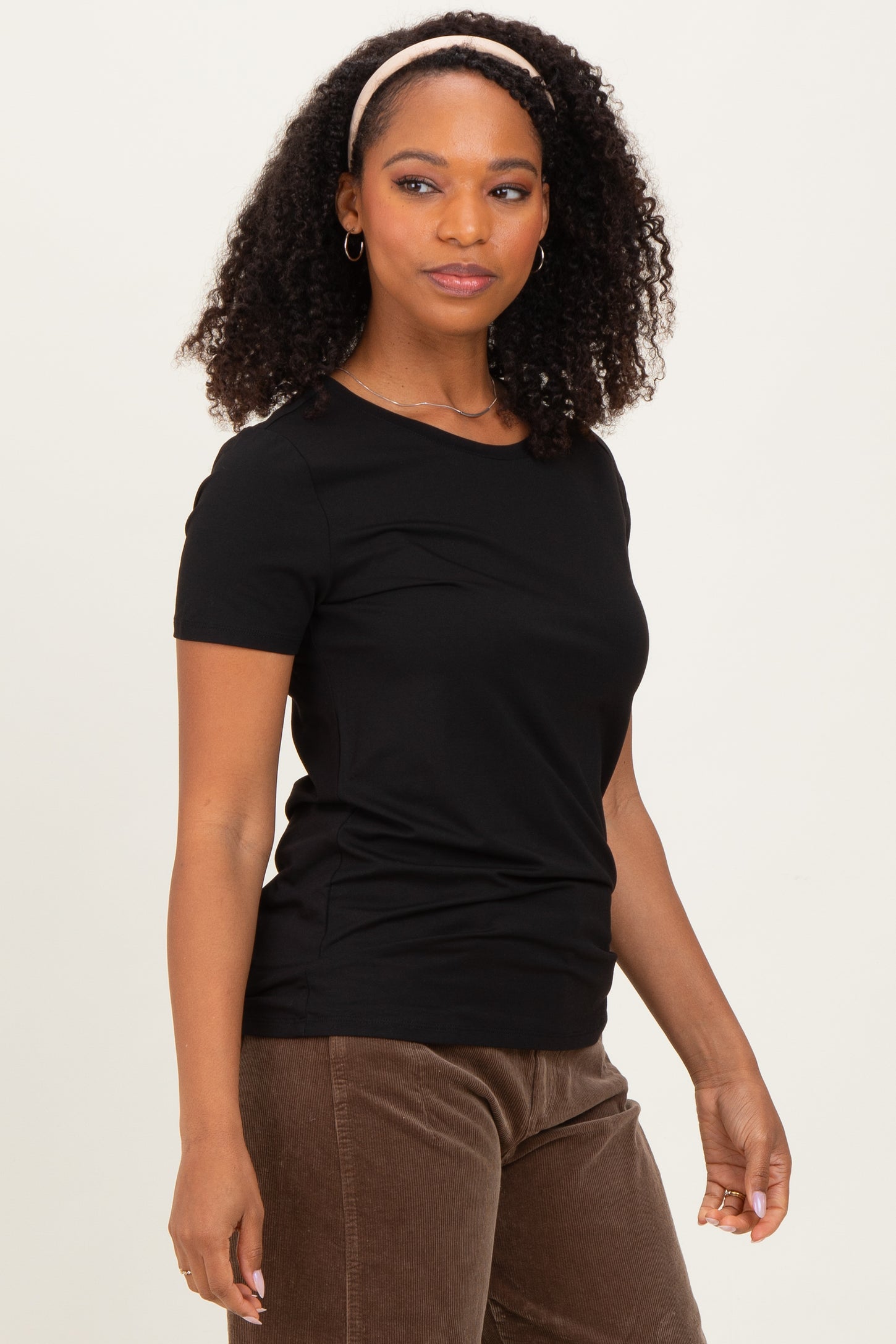 woman wearing a black short sleeve fitted t-shirt and brown corduroy pants, looking to the side
