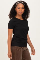 woman wearing a black short sleeve fitted t-shirt and brown corduroy pants, looking to the side