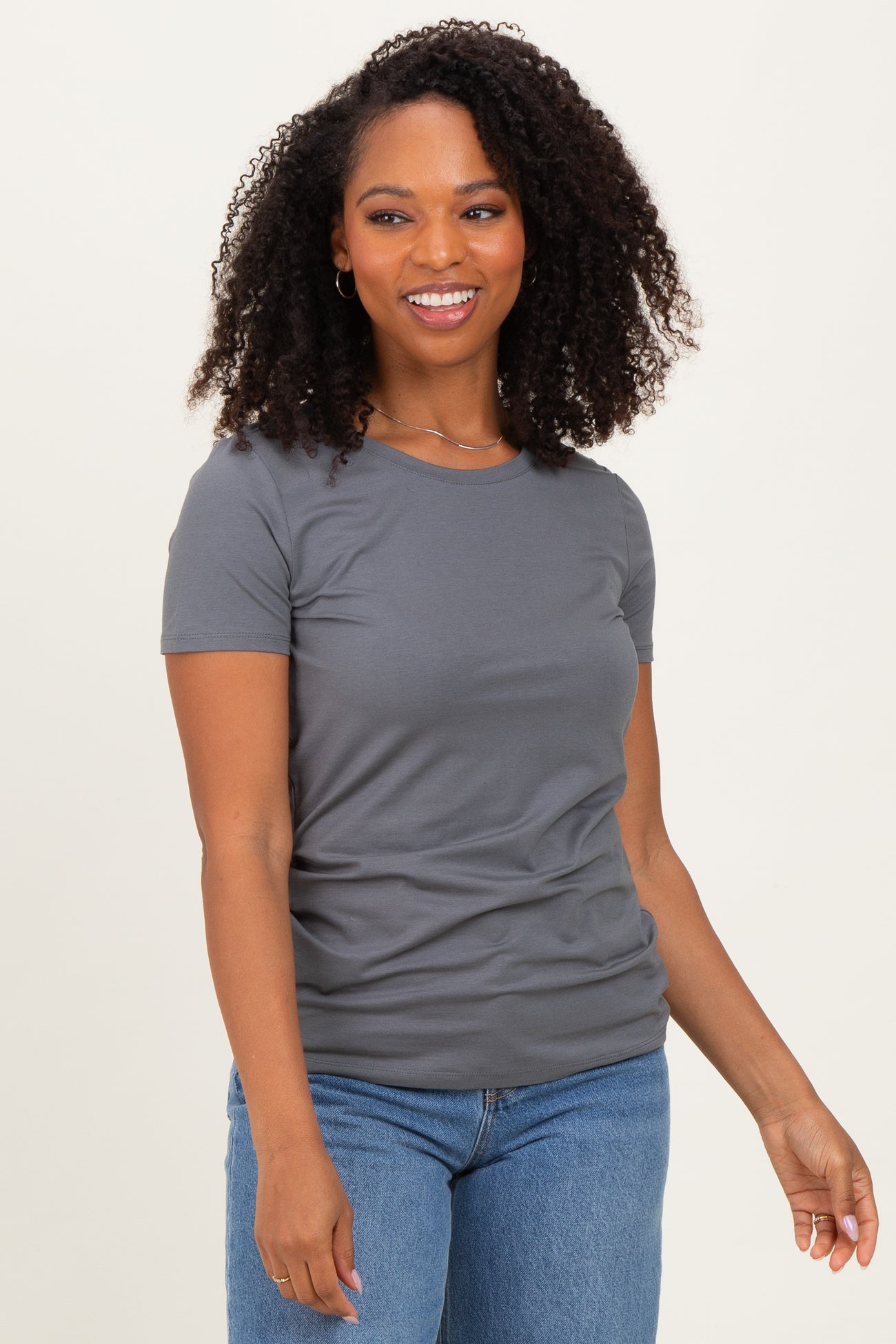 woman wearing a gray short sleeve t-shirt and blue jeans, smiling with curly hair