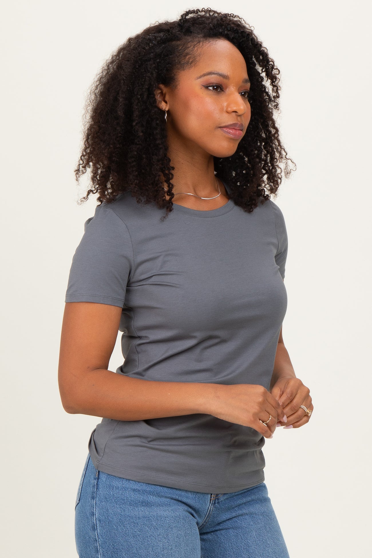 woman wearing a fitted gray short sleeve t-shirt and blue jeans, with curly hair and a side profile view