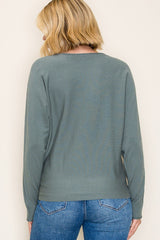 woman wearing a sage green long sleeve sweater, shown from the back, paired with blue jeans