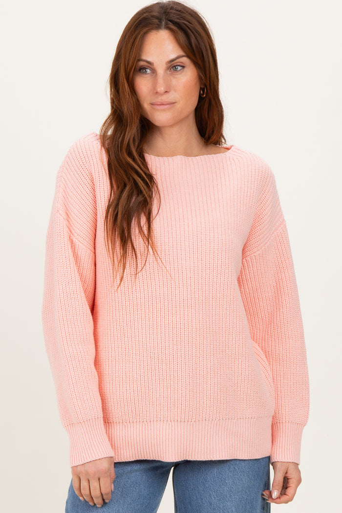 woman wearing a soft pink oversized knit sweater with a wide neckline and ribbed texture, styled with blue jeans
