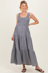 woman wearing a gray and white striped maternity maxi dress with a smocked bodice and tiered skirt, displaying her baby bump
