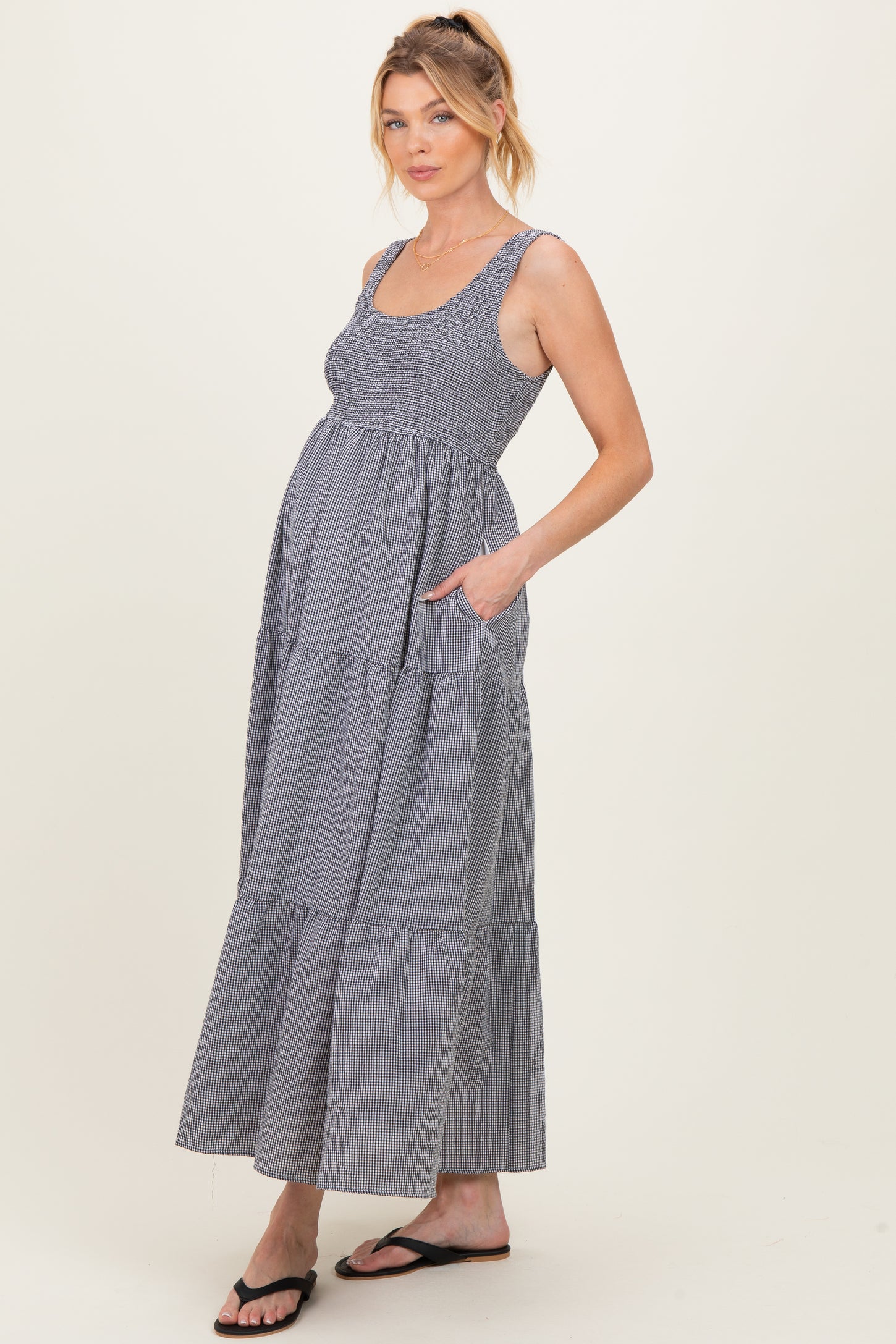 woman wearing a gray and white striped maternity maxi dress with a tiered design and pockets, showing her baby bump