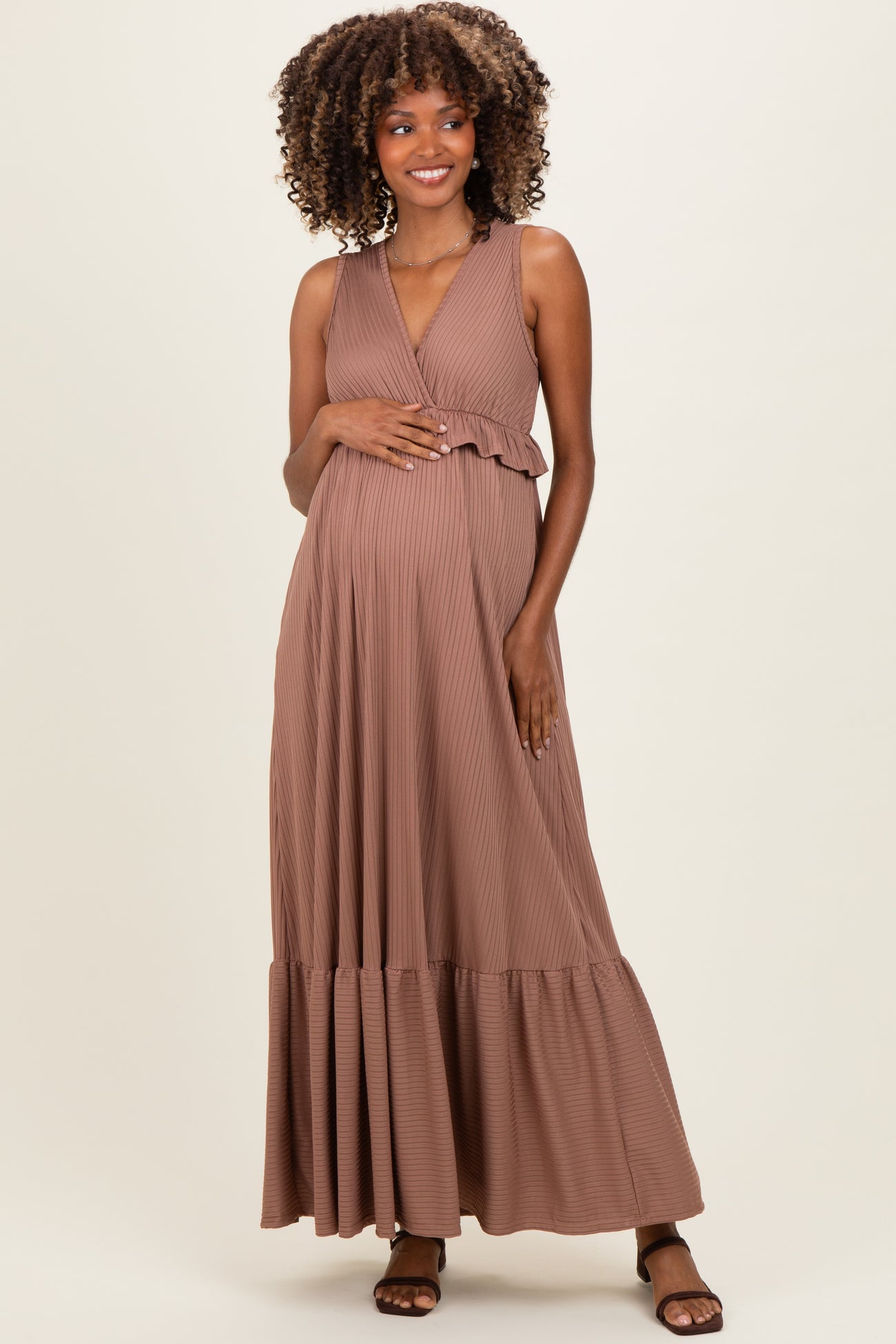 woman wearing a brown pleated maternity maxi dress, gently holding her baby bump