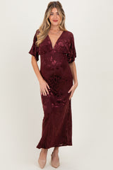woman wearing a burgundy floral velvet maternity gown with short flutter sleeves and a deep v-neckline, showing her baby bump