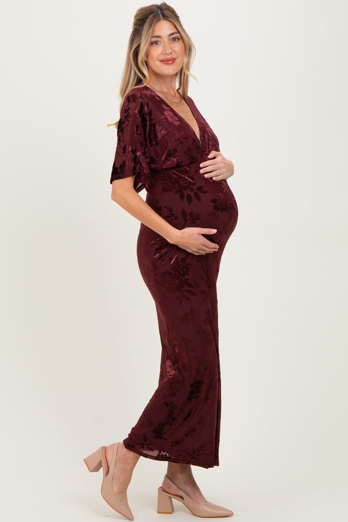 woman wearing a burgundy velvet maternity dress with floral design and holding her baby bump