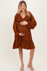 woman wearing a rust-colored v-neck maternity dress with puff sleeves and a ruffle hem, showing her baby bump