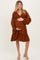 woman wearing a rust-colored v-neck maternity dress with puff sleeves and a ruffle hem, showing her baby bump