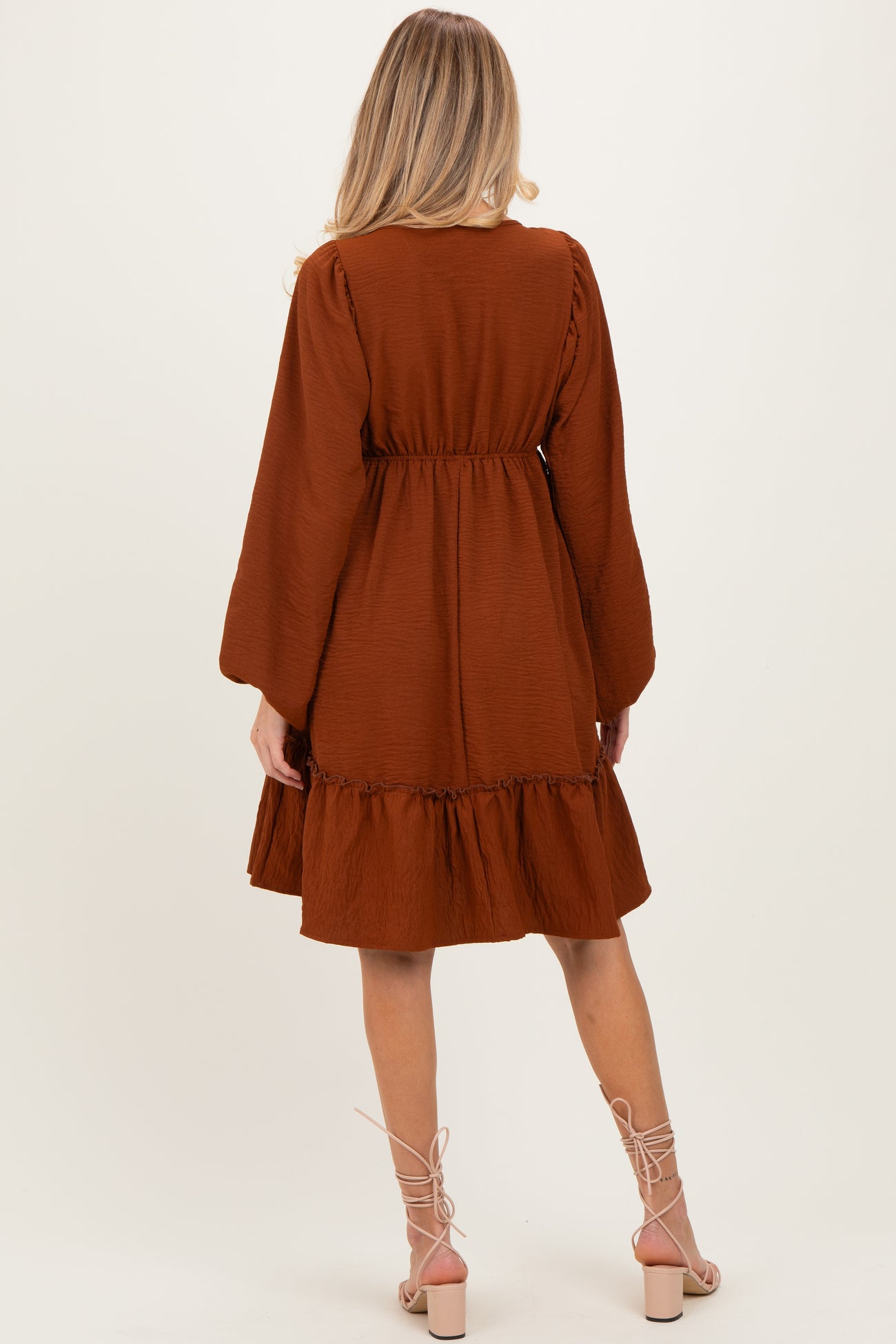 woman wearing a brown maternity dress with long sleeves and a ruffled hem, showing her back