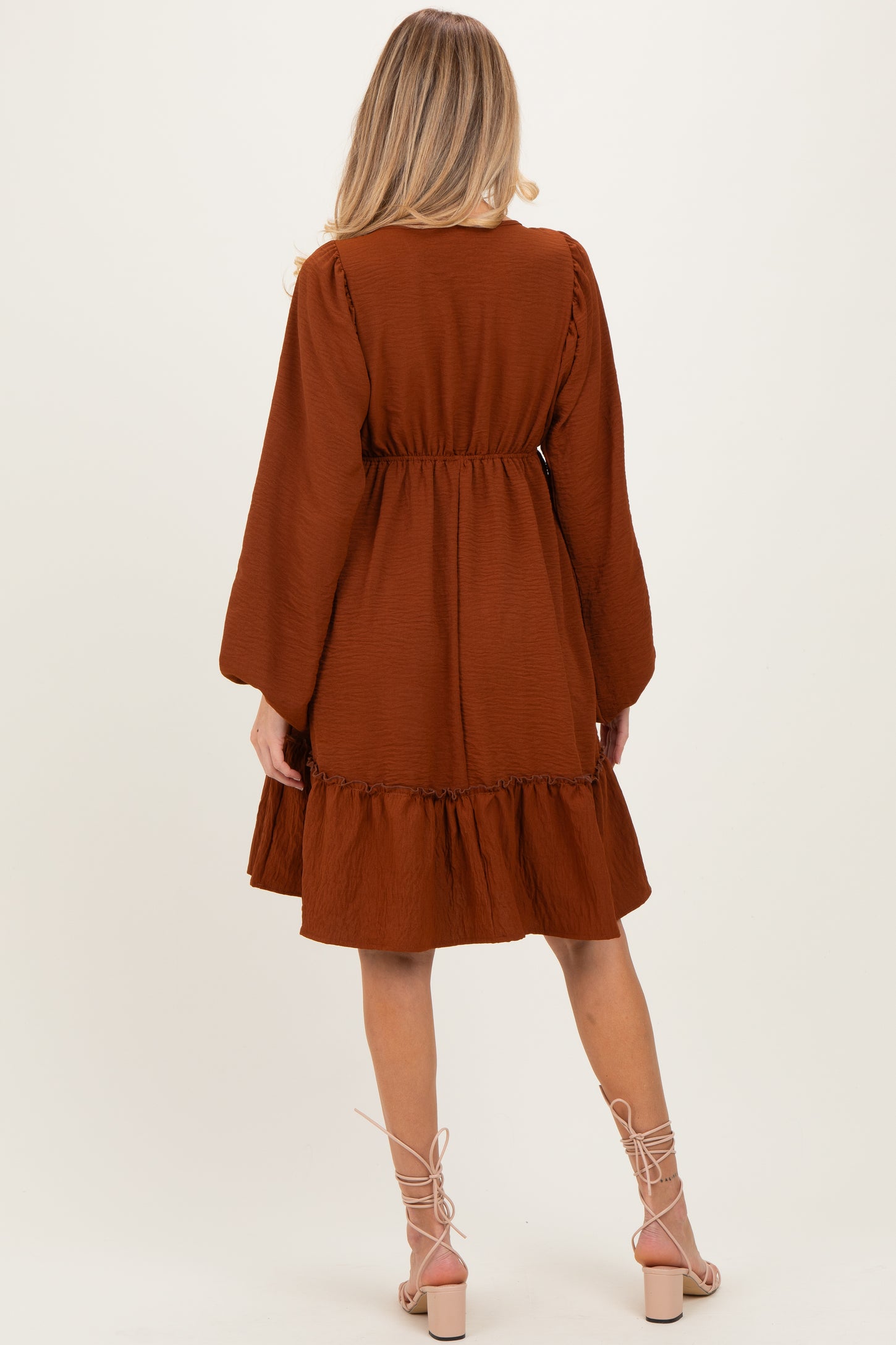 woman wearing a brown maternity dress with long sleeves and a ruffled hem, showing her back