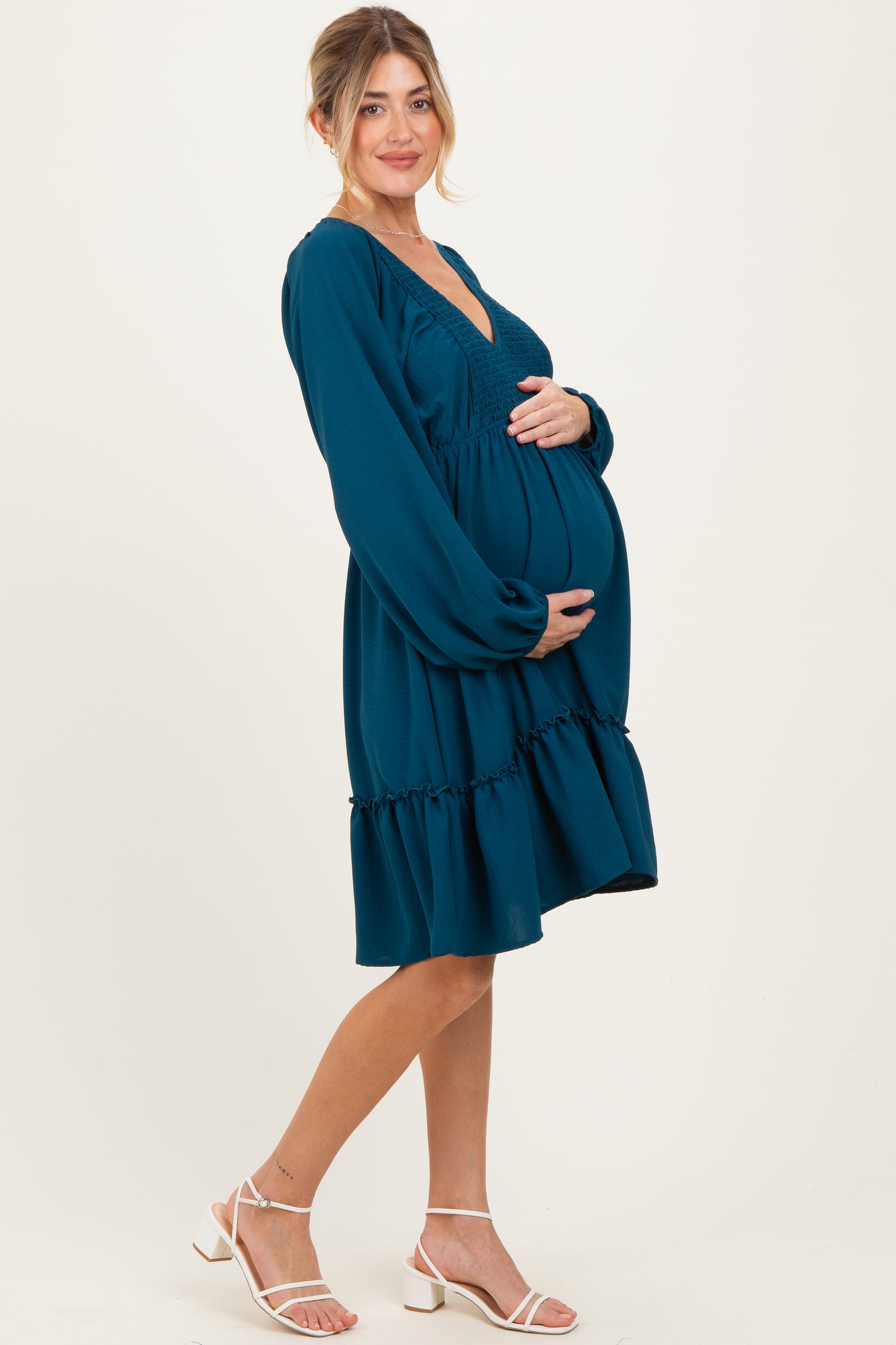 woman wearing a teal maternity dress with puff sleeves and ruffled hem, gently cradling her baby bump